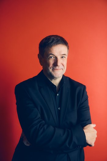 Autor vor rotem Huntergrund, lächelnd, schwarzes Hemd, kurze braune Haare